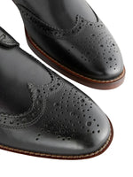 Close-up of black leather dress shoes with brown soles on a light background