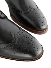 Close-up of black leather dress shoes with brown soles on a light background