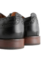 Black leather shoes with brown soles on a light background