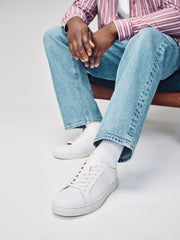 Person wearing light blue jeans, white sneakers, and a striped shirt sitting on a white background