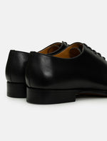 A pair of black leather derby dress shoes shown from a rear three-quarter angle against a light gray background.