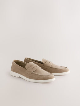 A pair of taupe suede penny loafers with white soles, displayed on a clean, light beige studio background.