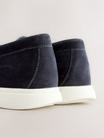 Close-up rear view of a pair of dark navy suede ankle boots with thick white platform soles, set against a light beige background.
