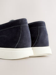 Close-up rear view of a pair of dark navy suede ankle boots with thick white platform soles, set against a light beige background.